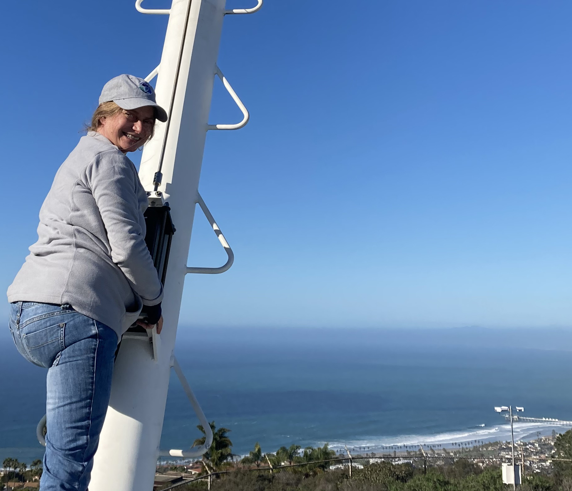 In early January 2023, EPCAPE Principal Investigator Lynn Russell works on her aerosol sampling van on Mount Soledad. To the far right, along the beach below, is Scripps Pier, the main site for ARM EPCAPE instrumentation. 