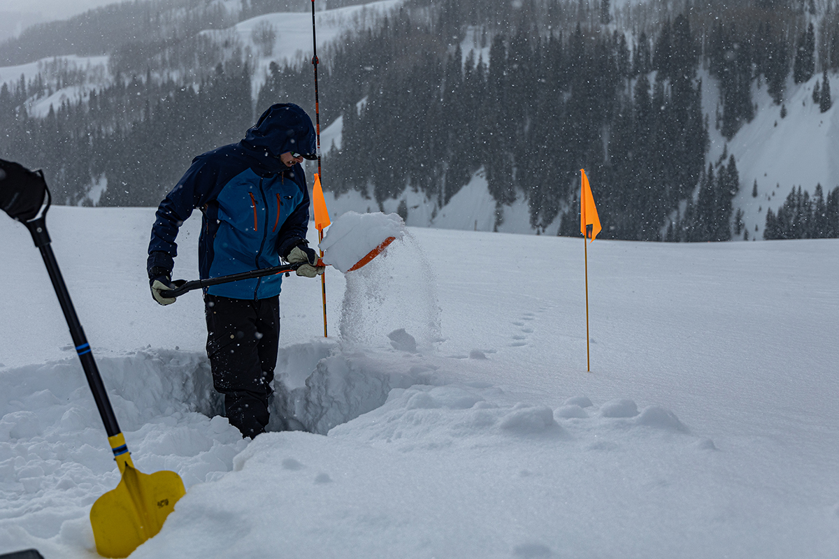 Schwat, a University of Washington PhD student, starts digging a snow pit, a deep rectangular hole used to measure snowpack properties.