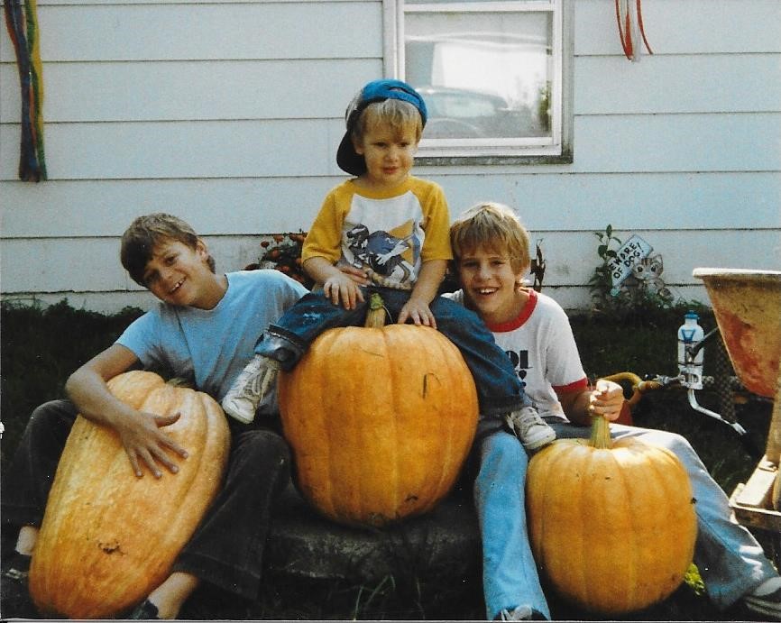 Theisen, around age 4, sits on a pumpkin at his family’s Minnesota dairy farm with his brothers Ryan (left) and Christopher (right). 