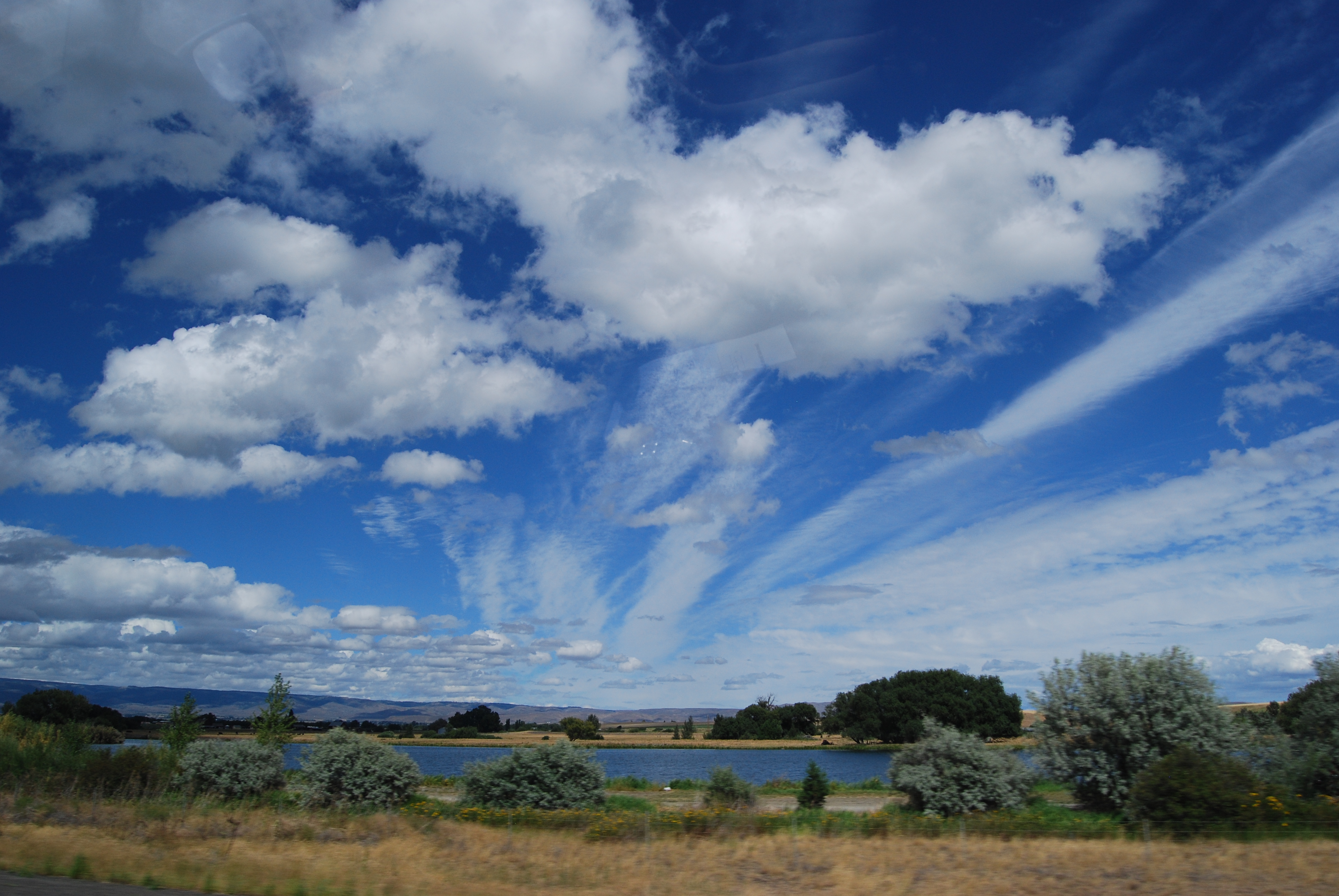 Lower altitude fluffy clouds compoused of water microdroplets and higher alttitude thin elongated clouds fill the sky over the Columbia River in Richland, Washington. Laskin investigates the composition and phyisical properties of the individual atmospheric particles that control processes of cloud formation and persistence. Photo is courtesy of Laskin. 
