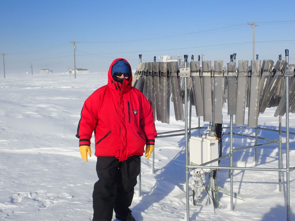 In 2019, at ARM’s North Slope of Alaska atmospheric observatory, atmospheric scientist Jennifer “Jen” Delamere dressed for the cold in her decades-old, Fairbanks-made Apocalypse Design parka during the Snow ALbedo eVOlution (SALVO) field campaign. She is next to a shield enclosing a laser precipitation monitor. The shield decreases wind flow over the instrument, increasing its sample-catch efficiency.