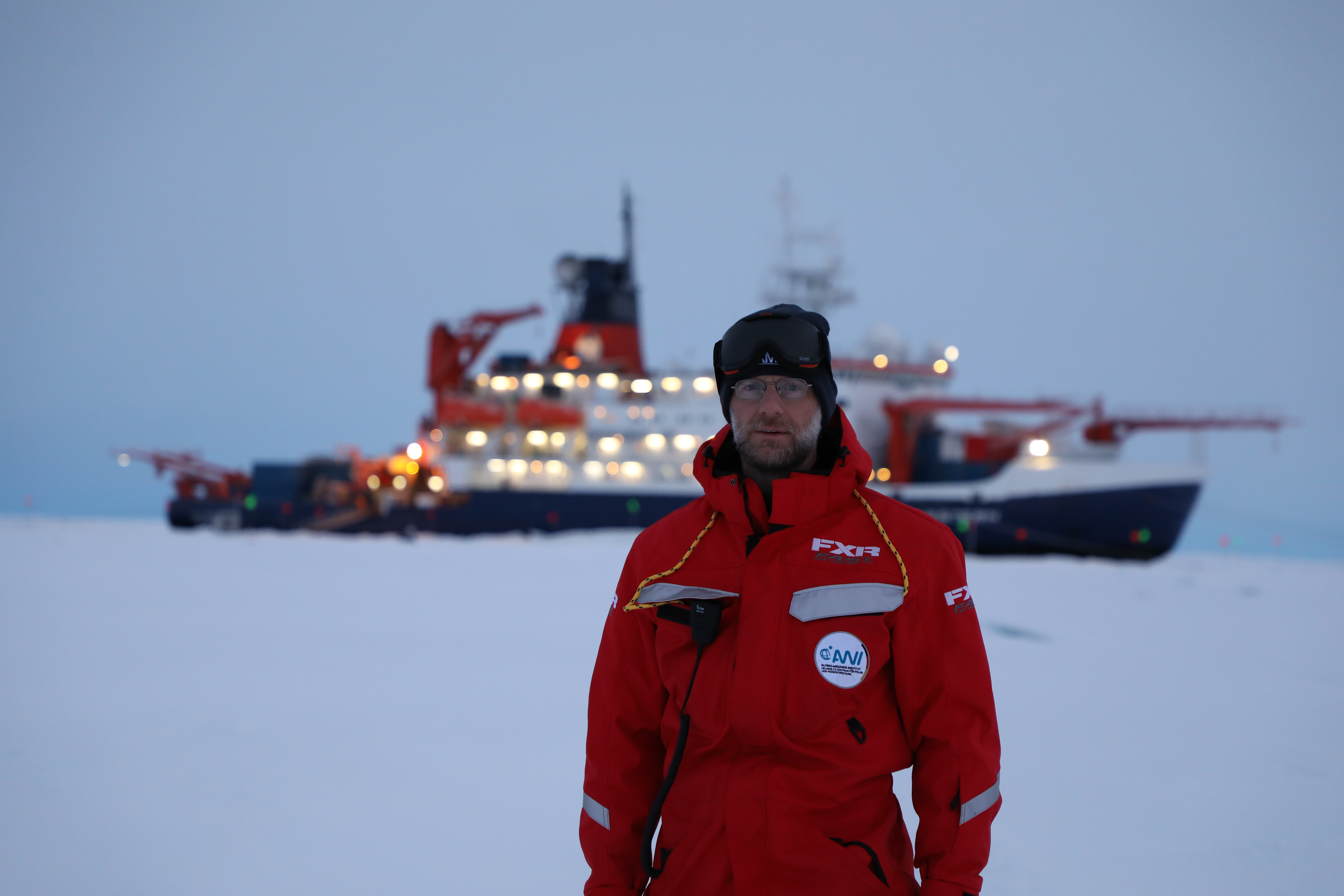 In the fall of 2019, Matthew Shupe poses on the ice in the central Arctic during the MOSAiC expedition. Behind him, moored to an ice floe, is the German research icebreaker R/V Polarstern. Its bow is stacked with ARM instruments for measuring cloud and atmospheric properties. 