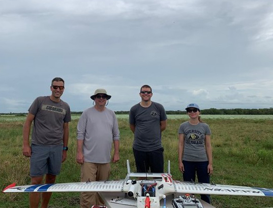On August 26, 2022, Jensen (second from left) visited a few members of the University of Colorado Boulder team in Brazoria County, Texas, for a TRACER-related campaign using uncrewed aerial systems. At the far left is lead scientist Gijs de Boer. At the far right is postdoctoral researcher Radiance Calmer; next to her is remote-sensing lab manager Michael Rhodes. The RAAVEN aircraft is in front. Photo is courtesy of Jensen.