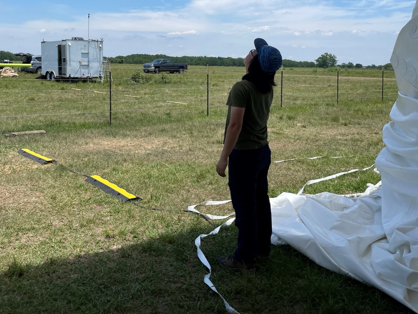 In July 2022, from the shade of a tethered balloon shelter in Guy, Brookhaven National Laboratory scientist Chongai Kuang watches one of his aerosol instruments borne aloft on a tethered balloon system.