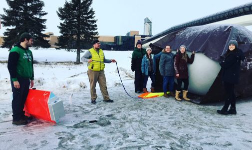 Aaron Kennedy, in the yellow vest, helps student prepare a helium-balloon platform packed with instruments on the University of North Dakota campus. 